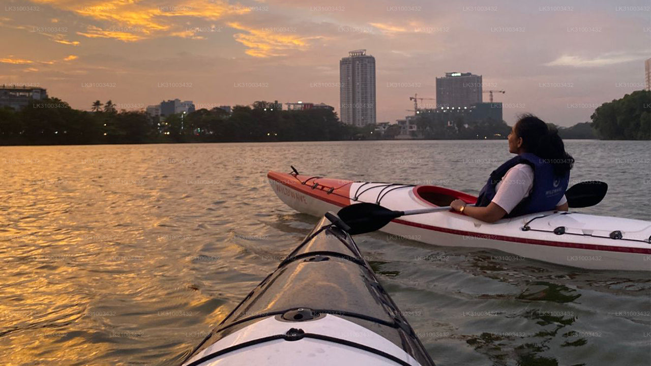 Person kayaking on a lake with city skyline in the background during sunset.