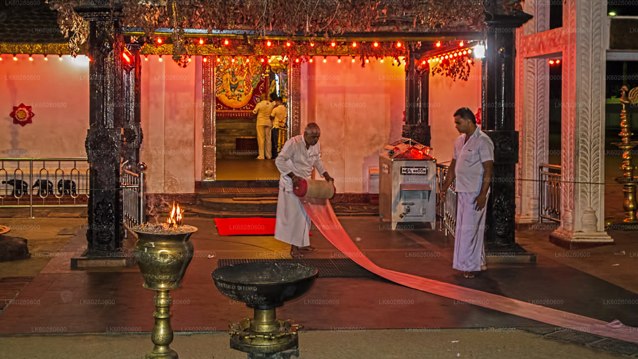 A group of people in traditional attire are seen inside a Hindu temple, with a man holding a large red cloth.