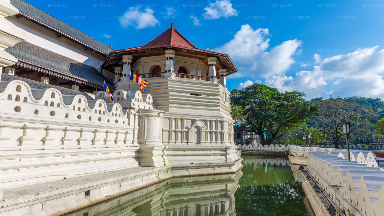 The image shows the exterior of the Temple of the Sacred Tooth Relic in Kandy, Sri Lanka, with its iconic white walls and red roof against a blue sky with clouds.